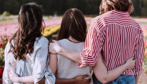 Tre ragazze di schiena si abbracciano con affetto