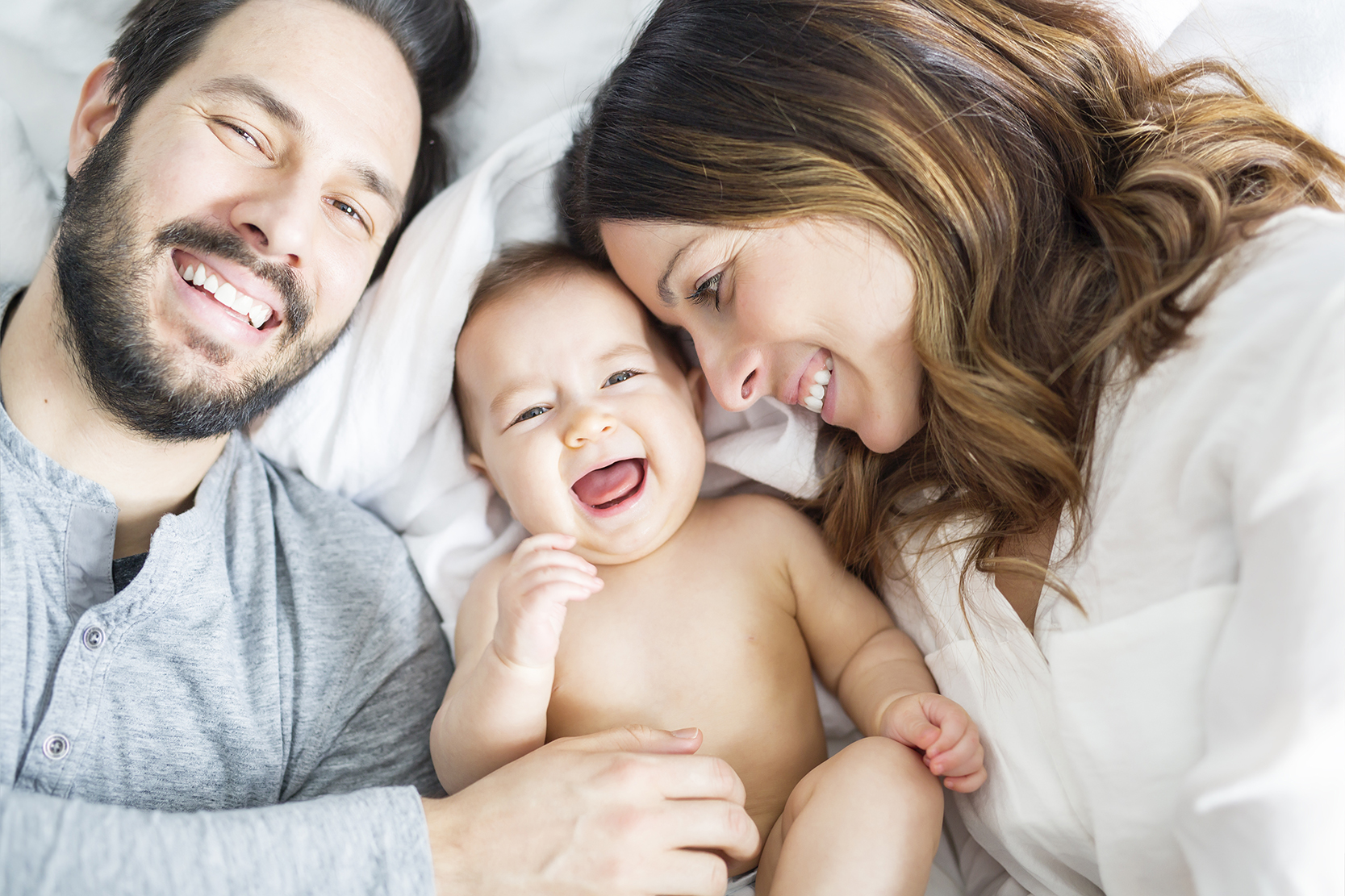 Padre, madre e neonato sorridenti sdraiati insieme su un letto